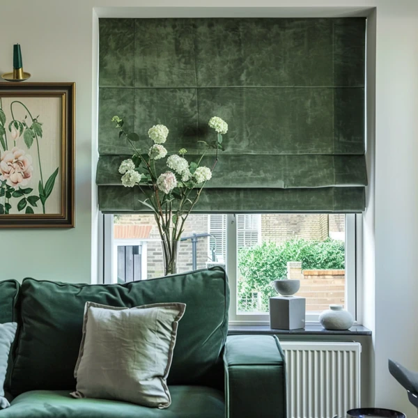 Green velvet roman blinds framing a window with plants